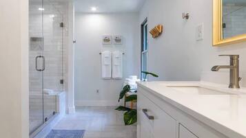Un baño moderno con cabina de ducha de vidrio, tocador blanco con grifo dorado y un espejo grande.