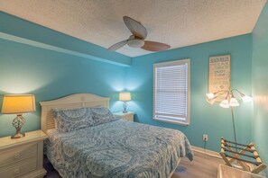 A bedroom with a bed, nightstands, a ceiling fan, a window with blinds, and a wall sign. - Sunchase 206| Pool & Hot Tub | Steps to the Beach (Gulf Shores)