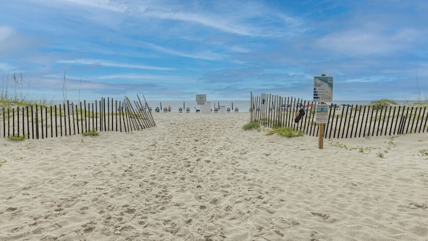 Una playa arenosa con una valla de madera y una torre de salvavidas a lo lejos.