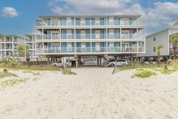 A beachfront motel with multiple balconies, a sandy beach in front, and several parked cars. - Sunchase 206| Pool & Hot Tub | Steps to the Beach (Gulf Shores)