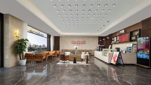 A hotel lobby with a reception desk, seating area, and a large window offering a city view. - Mövenpick By Accor Binjiang Nanjing (Nanjing)