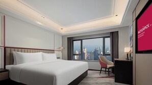 A modern hotel room with a large bed, a desk, a chair, and a city view. - Mövenpick By Accor Binjiang Nanjing (Nanjing)