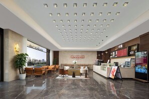A hotel lobby with a reception desk, seating area, and a large window offering a city view. - Mövenpick By Accor Binjiang Nanjing (Nanjing)