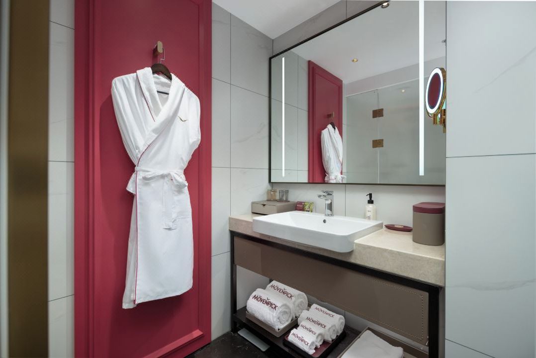 Un baño moderno con un lavabo blanco, un espejo grande y una pared de acento roja.