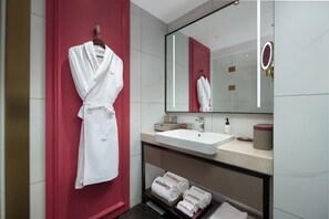 A modern bathroom with a white sink, a large mirror, and a red accent wall. - Mövenpick By Accor Binjiang Nanjing (Nanjing)