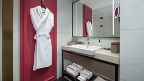 A modern bathroom with a white sink, a large mirror, and a red accent wall. - Mövenpick By Accor Binjiang Nanjing (Nanjing)