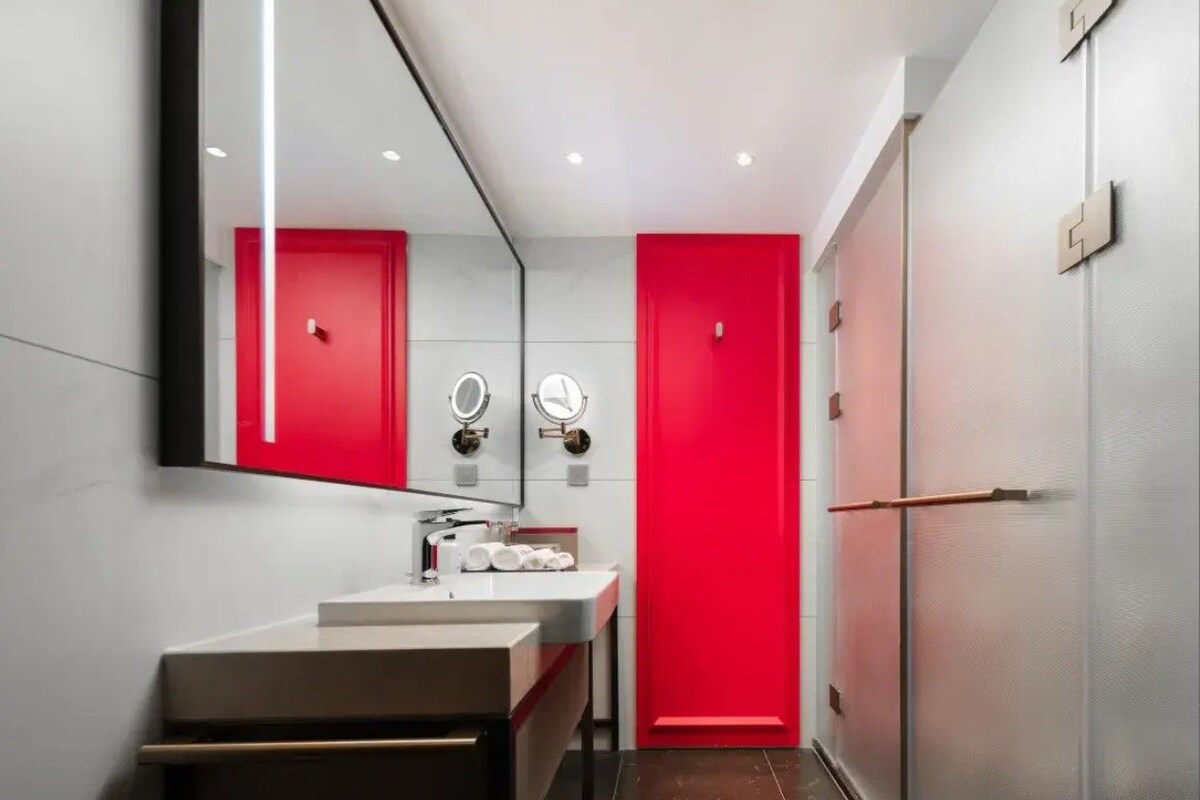 A modern bathroom with a white sink, two mirrors, and a red door.