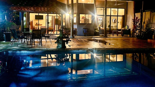 Ein modernes Haus mit Swimmingpool, Gartenmöbeln und einem gut beleuchteten Innenraum.