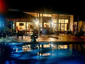 A modern house with a swimming pool, outdoor furniture, and a well-lit interior. - Arriba (upper) (Quepos)