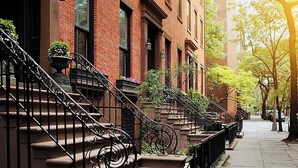 A row of brick townhouses with ornate black iron railings and potted plants on the stoops. - Kosher House (Brooklyn)