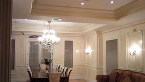 A dining area with a chandelier, a dining table with chairs, and a brown sofa. - Kosher House (Brooklyn)