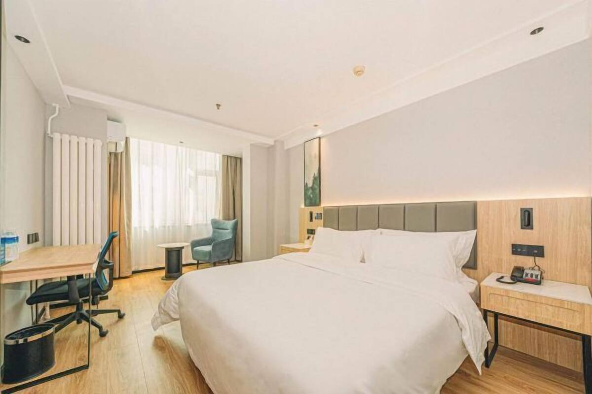 A hotel room with a large bed, a desk with a chair, a small table, and a nightstand with a lamp.
