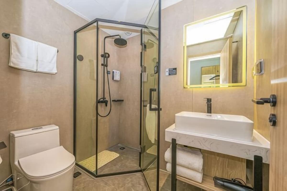 Un baño con ducha de vidrio, un lavamanos blanco y un espejo con marco iluminado.