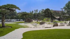 A landscaped garden with a winding path, large rocks, and a variety of trees. - GreenTree Inn Express Hotel (Beijing)