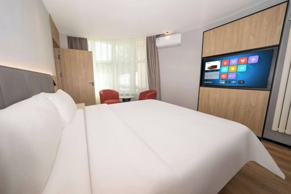 A modern hotel room with a large bed, a TV mounted on the wall, a small table, and a chair.