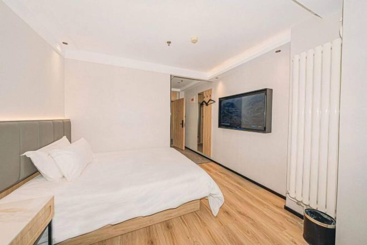 A bedroom with a bed, a bedside table, a wall-mounted TV, and a radiator.
