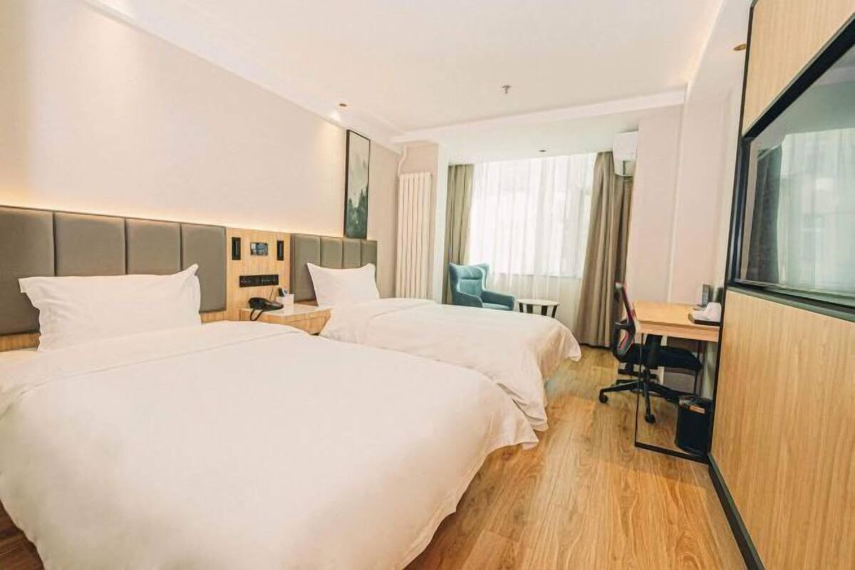 A hotel room with two beds, a desk, a chair, and a large window.