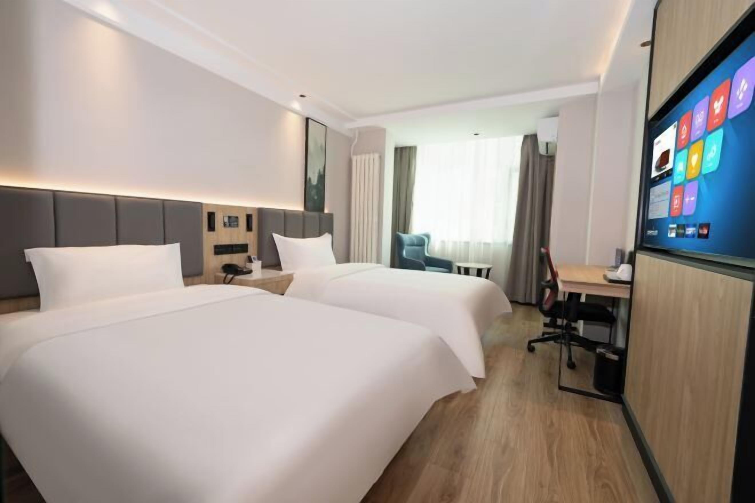 A hotel room with two beds, a desk, a chair, and a large screen displaying apps.