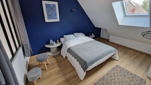 Et moderne soveværelse med skråvæg, en seng med hvidt sengetøj, et lille rundt bord med to barstole og et ovenlys.