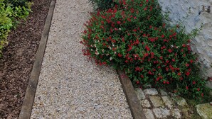 En bygning med facade af sten, grussti og røde blomsterplanter.