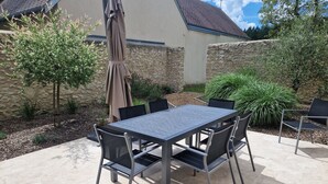 En terrasse med et bord og stole, omgivet af planter og en stenvæg.