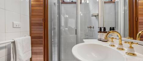 A modern bathroom with a glass shower enclosure, a white sink with gold fixtures, and wooden paneling on the walls.