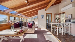 A spacious room with a high ceiling, wooden beams, a sofa, a dining table, and a kitchen area. - Nowhere Apartment Crackenback (Crackenback)