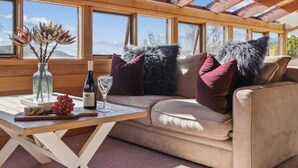 A cozy room with a wooden interior, a cushioned sofa, a table with a bottle of wine, a glass, and decorative items. - Nowhere Apartment Crackenback (Crackenback)