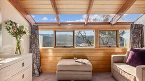A cozy room with wooden walls, a cushioned bench, a sofa, and a window overlooking a mountainous landscape. - Nowhere Apartment Crackenback (Crackenback)