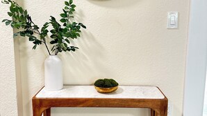 A wooden console table with a white vase and a green plant beside it, against a textured wall with a round mirror above.