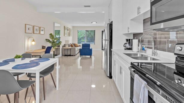 A modern kitchen with white cabinets, stainless steel appliances, and a dining area with a table and chairs.