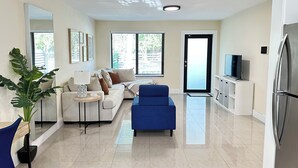 A modern living room with a sofa, blue armchair, and a flat-screen TV on a cabinet.