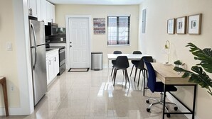 A modern kitchen with stainless steel appliances, a dining area with a table and chairs, and a small trash bin.