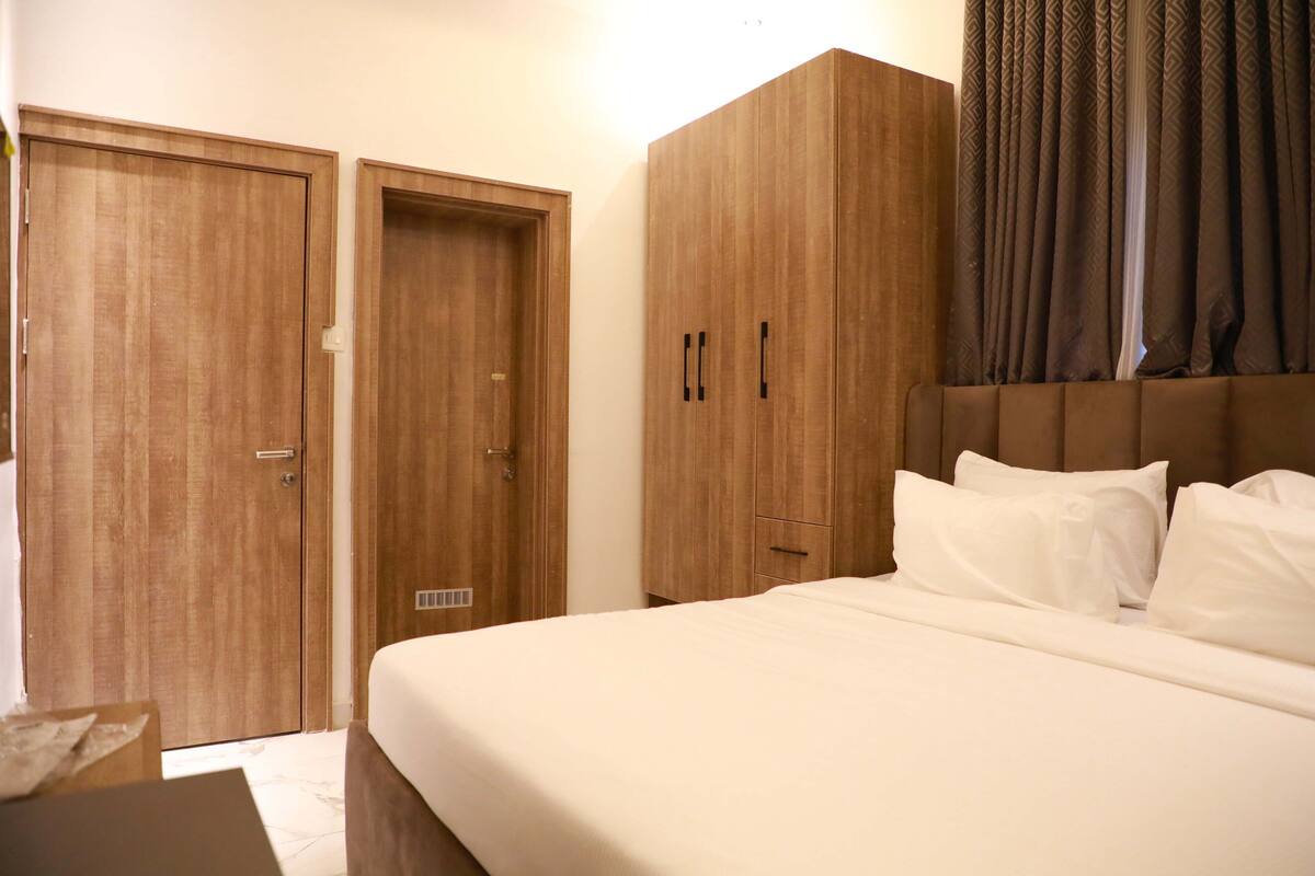 A hotel room with a large bed, wooden wardrobe, and a small table.