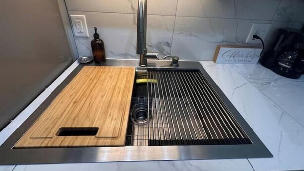 Een keuken met een inbouwgootsteen, een houten snijplank, een fles en een koffieapparaat.