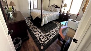Een slaapkamer met een hemelbed, een bureau met lamp, een radiator en een raam met gordijnen.