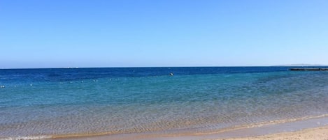 A beach with clear blue water and a sandy shore.