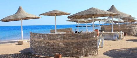 A beach with thatched umbrellas and wicker furniture.