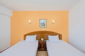 Ein Hotelzimmer mit einem Holz-Kopfteil, zwei Betten, einem Nachttisch mit Telefon und Wandleuchten.