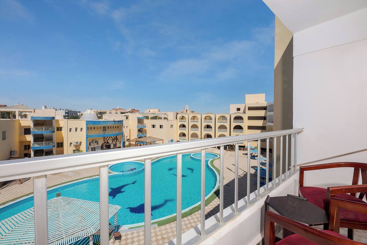 A pool area with a clear view of the surrounding buildings and a balcony with a table and chairs.