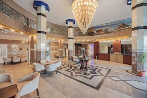 Eine geräumige Lobby mit Marmorböden, einem prunkvollen Kronleuchter und verschiedenen Sitzbereichen.