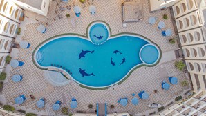 An aerial view of a resort with a large central pool featuring dolphin shapes, surrounded by checkered flooring and outdoor seating areas. - Saint Maria Hotel Hurghada (Hurghada)