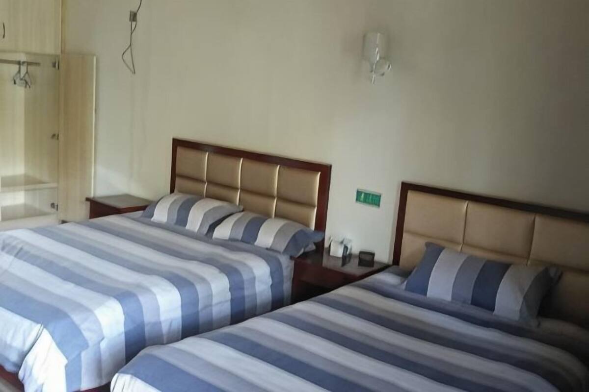 Two beds with striped bedding, a wooden headboard, a nightstand with a lamp, and a wall-mounted light fixture.