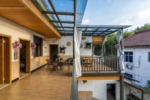 Un espace extérieur abrité, doté d’un plancher en bois, d’une table et de chaises, et d’un escalier menant à un niveau supérieur.