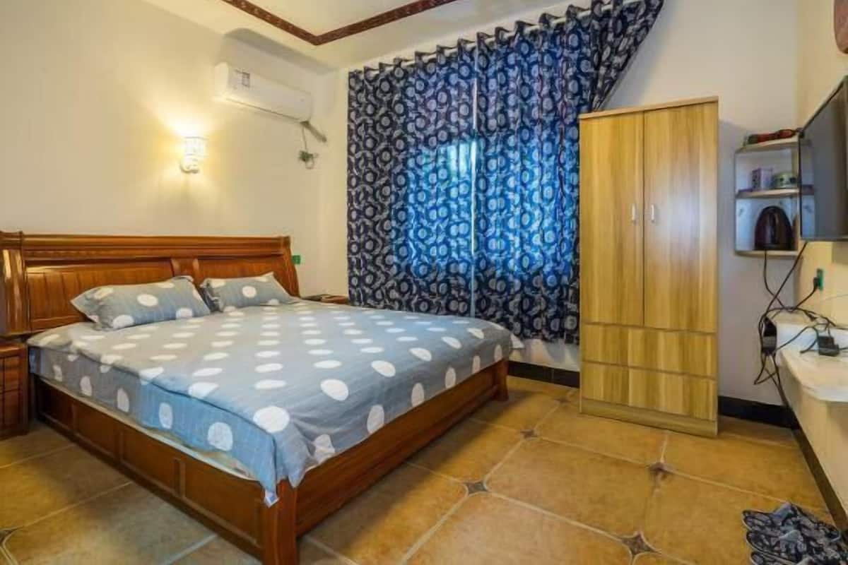 A bedroom with a wooden bed, patterned curtains, a wardrobe, and a tiled floor.