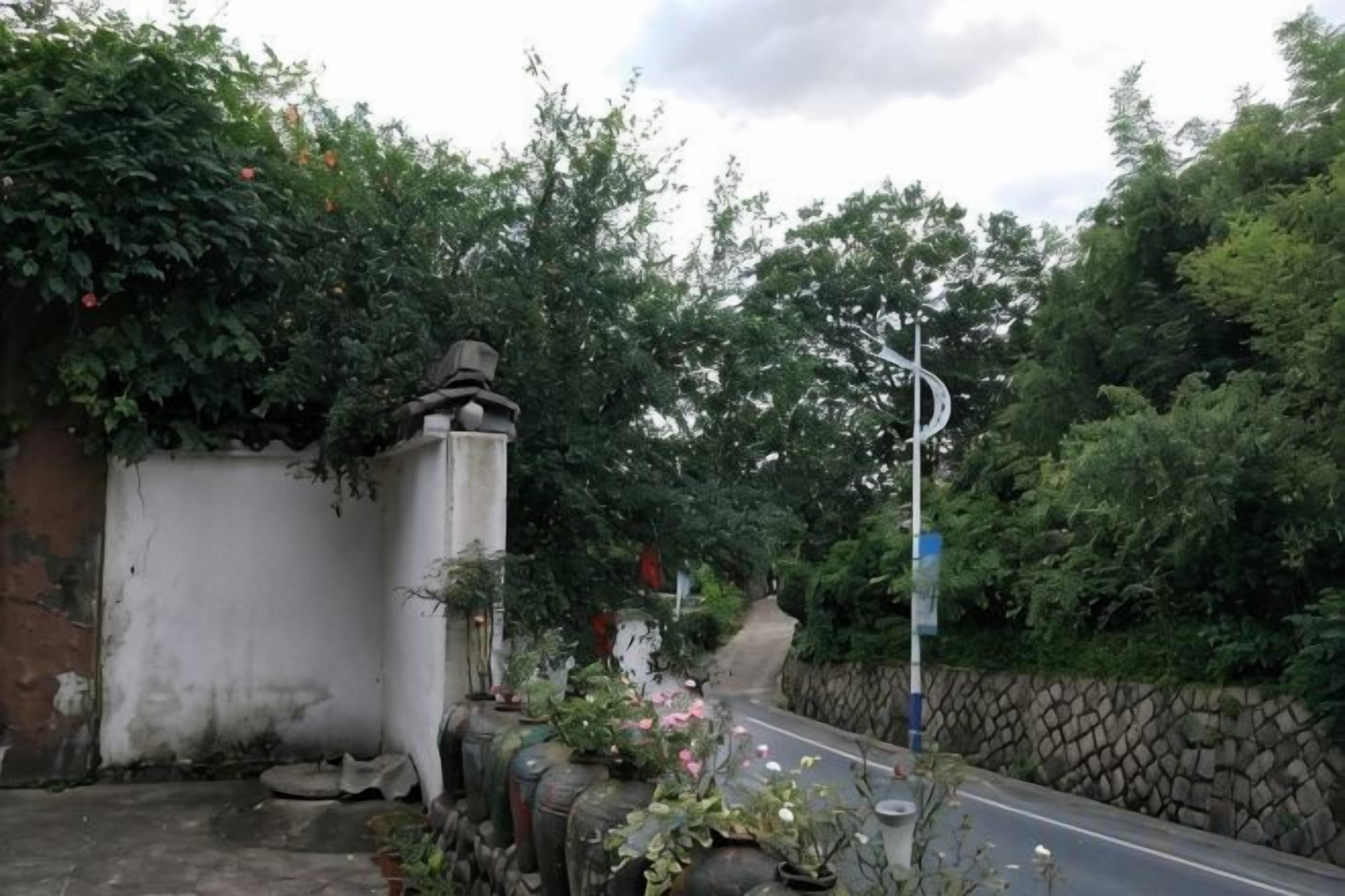 A residential street with a white wall, a stone wall, and a metal gate.