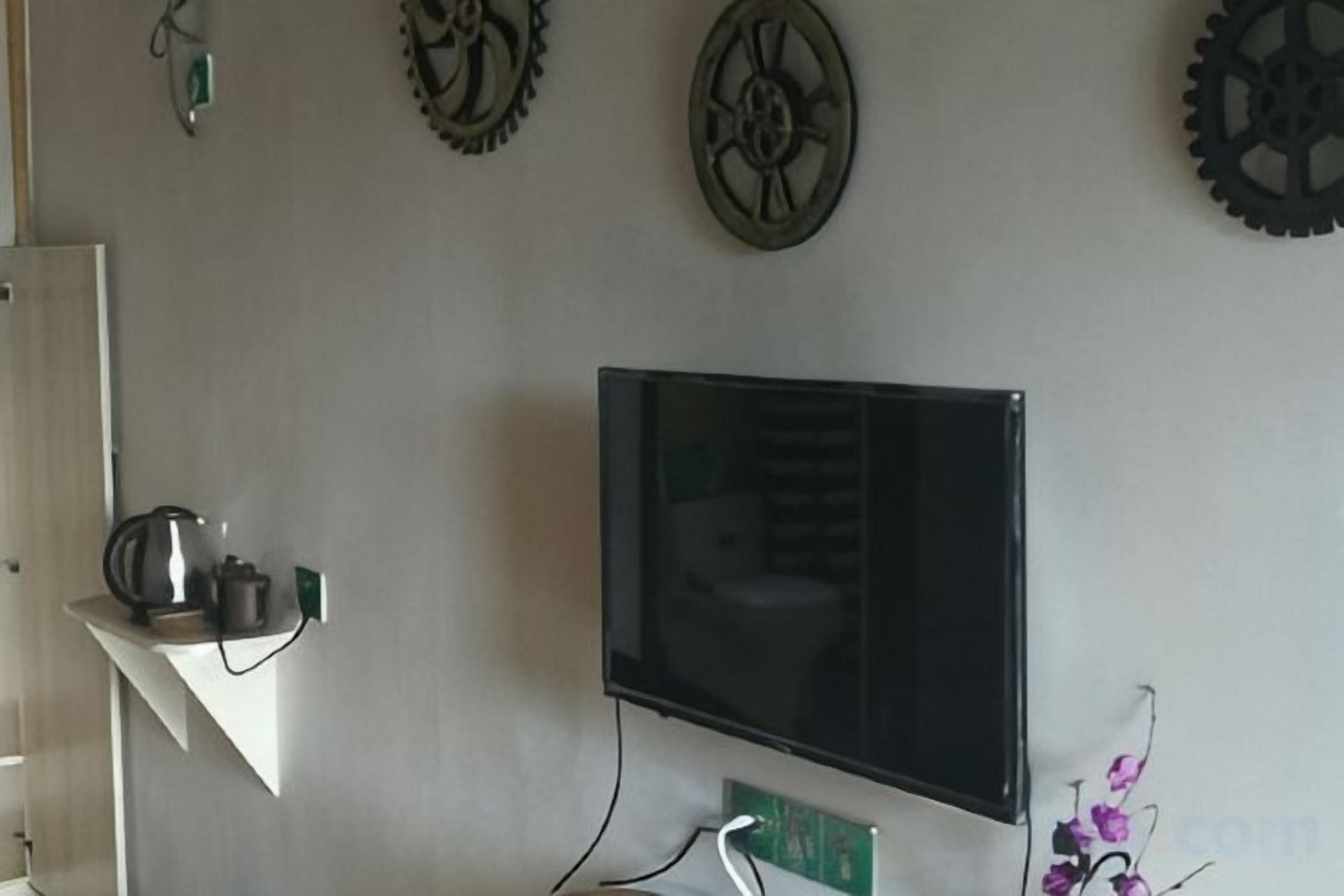 Un televisor de pantalla plana montado en la pared, un estante con un hervidor y una taza, y placas decorativas en la pared.