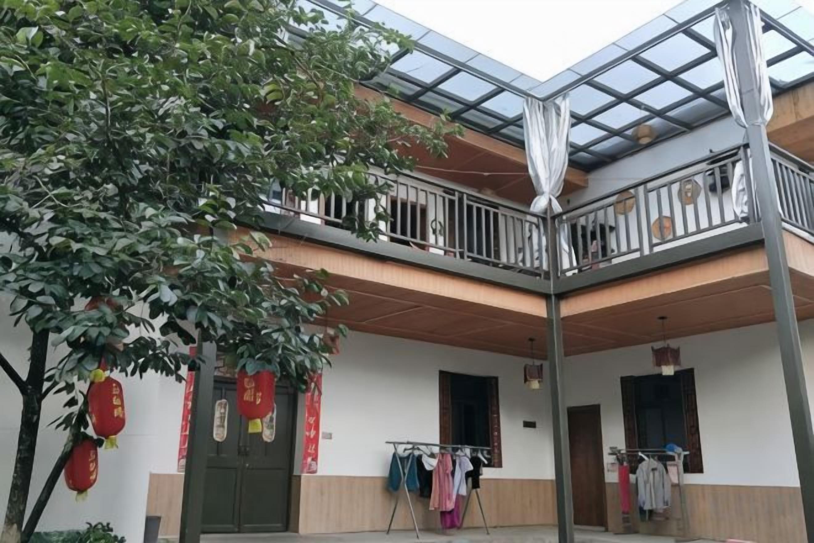 A two-story building with a balcony on the upper floor, a tree in the foreground, and a clothesline with garments.