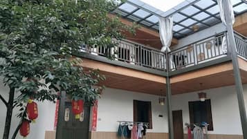 A two-story building with a balcony on the upper floor, a tree in the foreground, and a clothesline with garments.