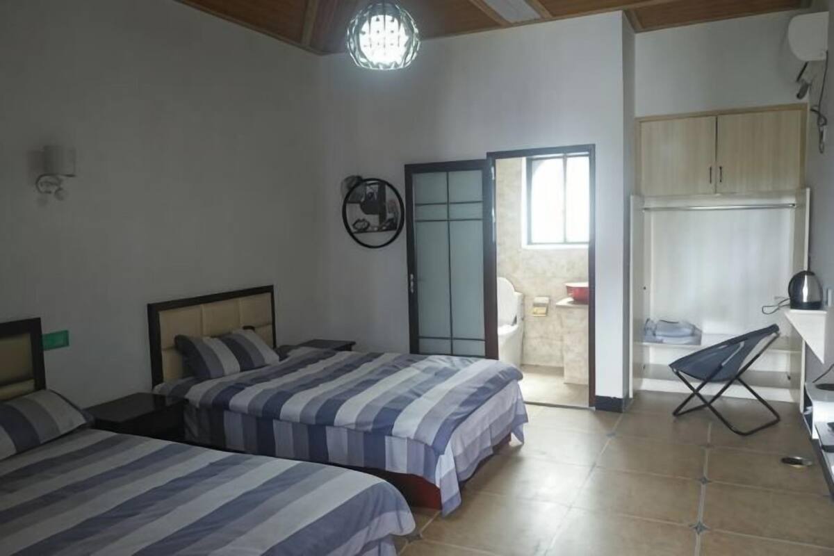 A bedroom with two beds, a small desk, a chair, a wardrobe, and a sliding door leading to a bathroom.